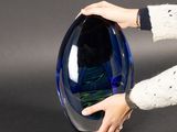 a person holding a blue glass vase on a black surface