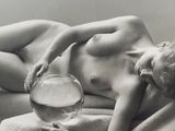 a naked woman laying on a bed with a fish bowl