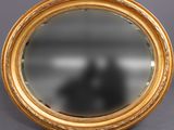 un miroir ovale avec un cadre doré posé sur une surface grise