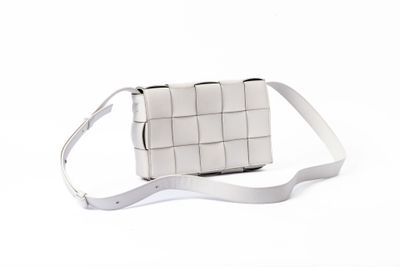 la bandoulière d'un sac à main blanc sur un fond blanc, posée sur une surface blanche