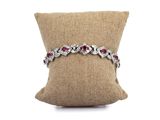 un bracelet en diamants et rubis posé sur un coussin, sur fond blanc