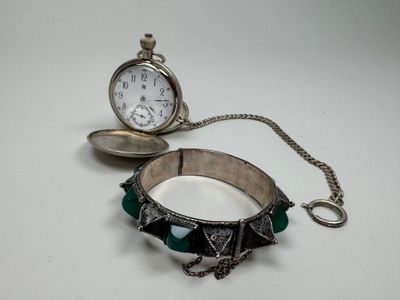 un bracelet argenté et vert avec une horloge en arrière-plan