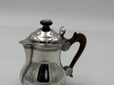 a silver teapot with a wooden handle on a white surface