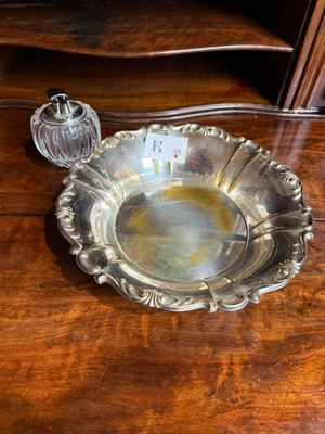 un plat en argent ancien posé sur une table en bois, à côté d'une bouteille en verre