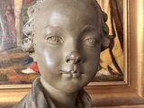a statue of a boy that is sitting in front of a painting