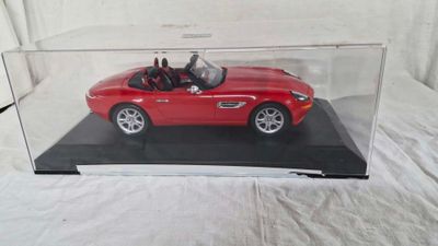 une petite voiture rouge dans une vitrine transparente posée sur une surface blanche
