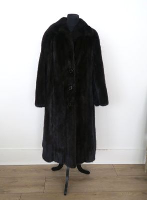 un manteau de fourrure noir posé sur un mannequin devant un mur blanc