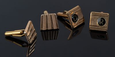 three gold cufflinks with black stones on a black surface