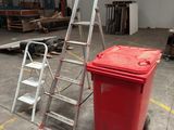 a red trash can next to a ladder in a warehouse