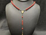 a necklace with a gold cross and red beads on a mannequin