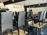 Des tables et des chaises sont alignées dans un restaurant, avec un bar en arrière-plan.