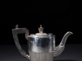 a silver teapot on a black surface with a black background