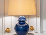 a blue vase sitting on a table with a lamp on top of it