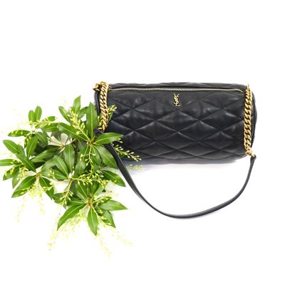 black quilted purse with gold chain strap next to a green plant