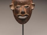 a wooden mask on a black stand with a white background
