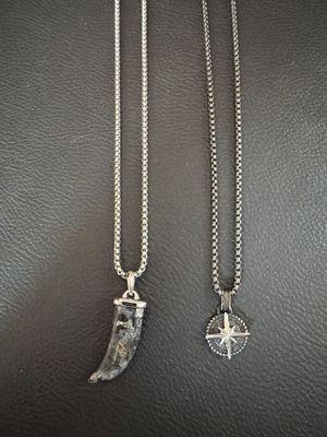 two silver necklaces with a shark tooth pendant on a black leather surface