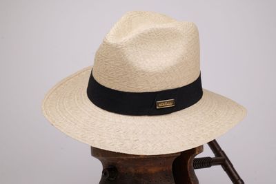 chapeau beige orné d'un ruban noir et d'un autre ruban noir, posé sur un support en bois