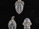 un ensemble de trois masques sculptés posés sur une surface noire