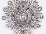 a silver brooch with a face surrounded by stars