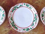trois assiettes ornées de feuilles de houx et bordées de rouge sont posées sur une table