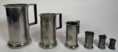un pichet en argent et quatre autres coupes en argent posés sur un plateau blanc