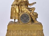 a gold clock with a man and a woman on it