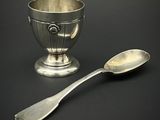 une tasse en argent et une cuillère posées sur une table noire