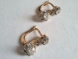 deux paires de boucles d'oreilles en or et diamants posées sur une surface blanche