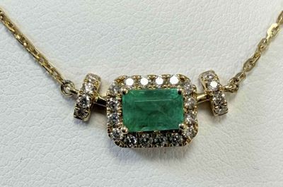 a close up of a necklace with a green stone surrounded by diamonds