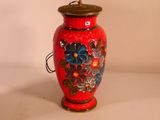 a red vase with flowers painted on it on a table