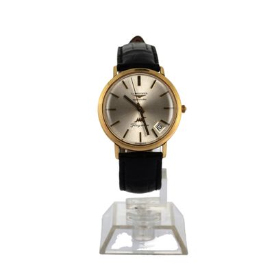 une photo d'une montre dorée et noire posée sur un socle transparent