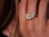 close up of a woman ' s hand holding a yellow and white diamond ring