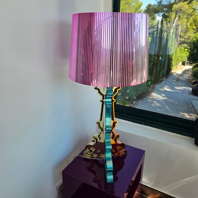 une lampe violette posée sur une table violette devant une fenêtre