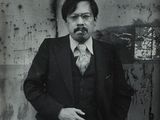 black and white photograph of a man in a suit and tie standing in front of a wall