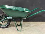 a green wheelbarrow is sitting on a concrete floor