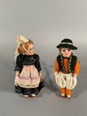two porcelain dolls of children dressed in traditional clothing and hats