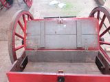 a red wagon with a wooden seat sitting on the street