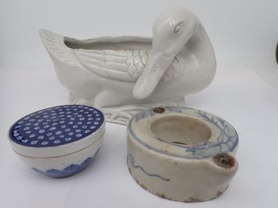 un canard blanc assis à côté d'un bol et d'un récipient bleu et blanc