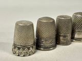 four antique thimbles lined up in a row on a white surface