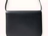 the black leather shoulder bag is on a white surface