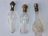 trois bouteilles en verre avec des bouchons dorés et un bouchon doré posé sur une surface blanche