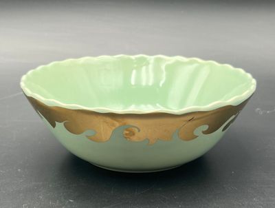 a green bowl with gold decoration on it on a table