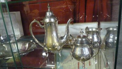 une théière en argent et une autre théière en argent posées sur une étagère en verre