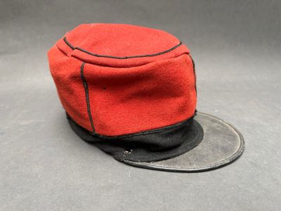 un vieux chapeau rouge et noir orné d'un ruban noir sur le dessus