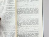 someone is holding an open book in their hand on a table