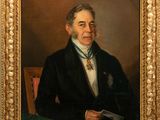 portrait of a man in a black suit and tie sitting at a table