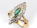 gros plan d'une bague en or avec une pierre verte et des diamants