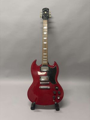 Une guitare électrique est posée sur un support, sur une surface blanche.