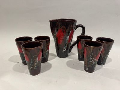 six verres rouges et noirs et un pichet posés sur un plan de travail blanc