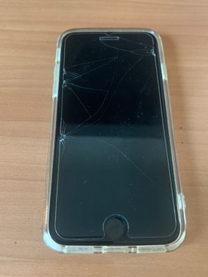 an iphone with a cracked screen sitting on a wooden table